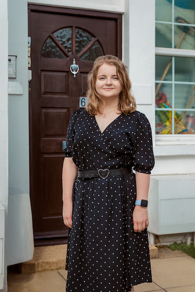 White woman in black dress in front of wooden front door