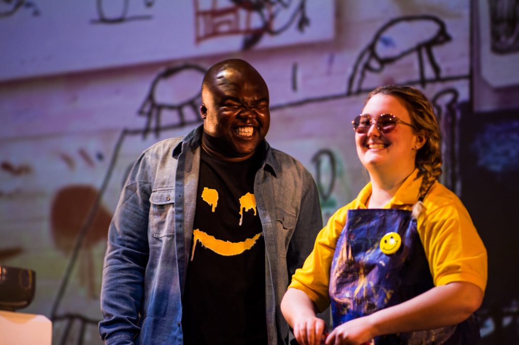 Black man and whote woman wearing tops with smiley faces on them grin broadly