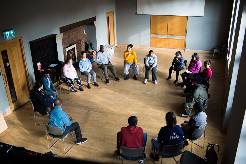 People sit in a circle in room with wooden floor